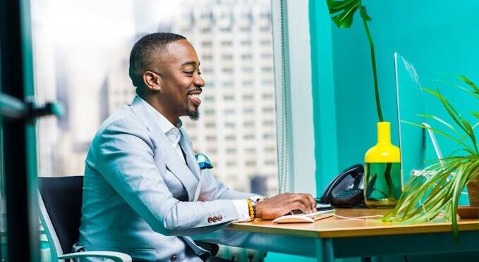 Confident businessman in modern office working on laptop with city view.