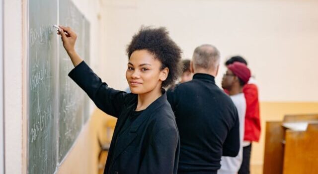 A student writing confidently on a blackboard in a lively classroom setting with peers.